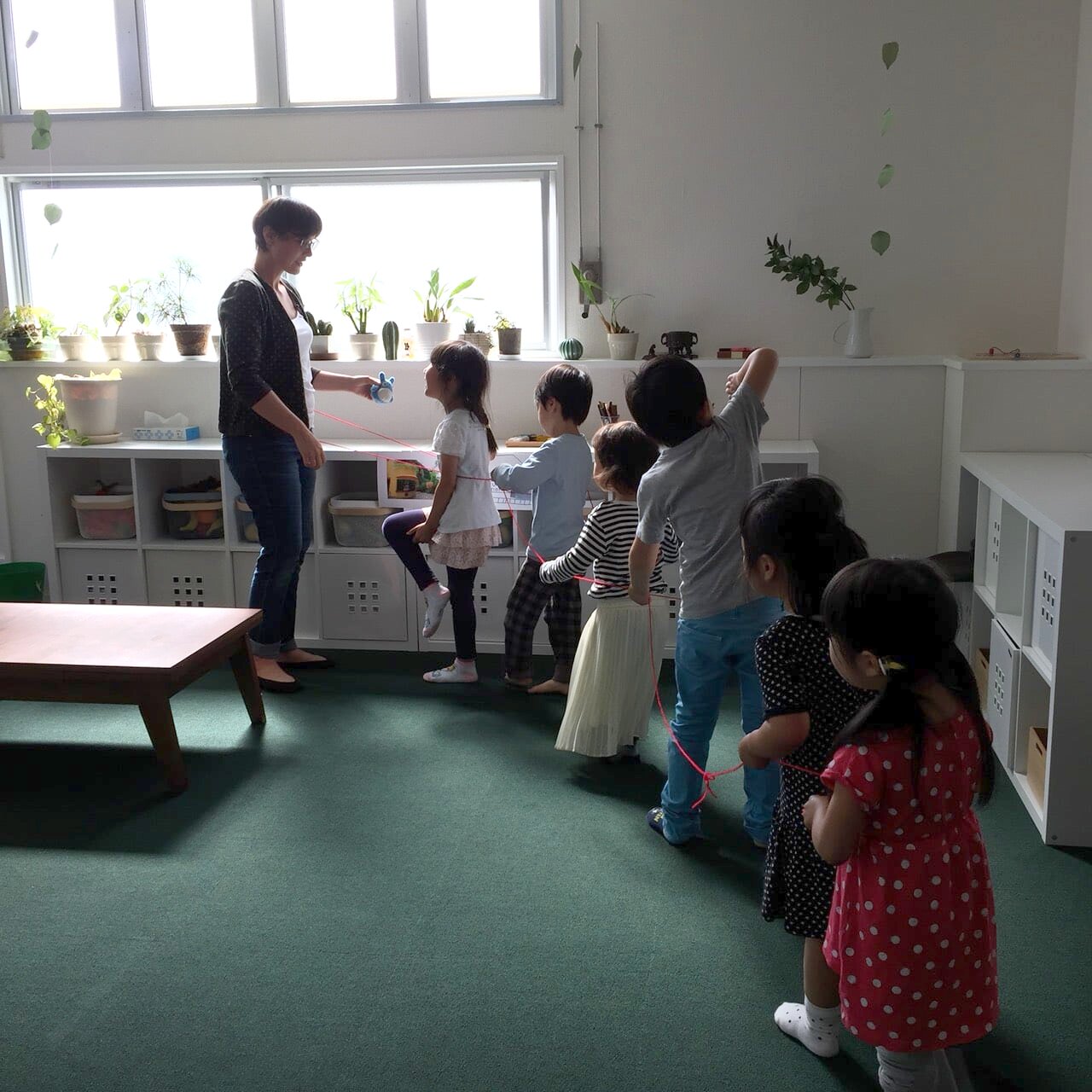 ひもを持って一列につながるアクティビティをする幼児たちと先生